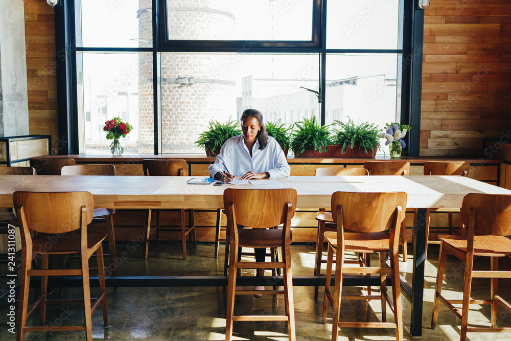 Fototapeta premium Woman sitting by a desk while reviewing business files in coffee shop