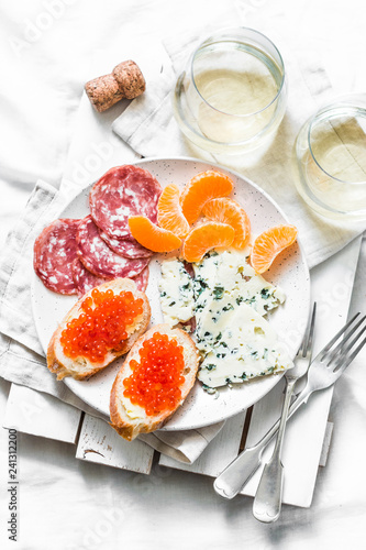 Delicious appetizer - red caviar sandwiches, blue cheese, salami, tangerines and white wine on a light background, top view. Flat lay