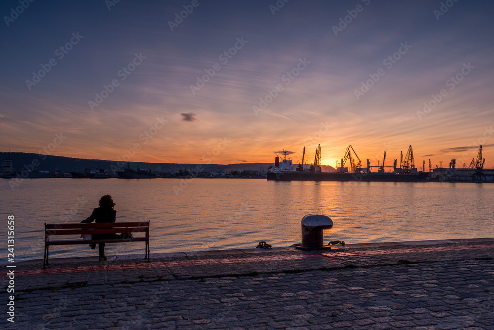 Girl watches the sunset at the sea station with ships.