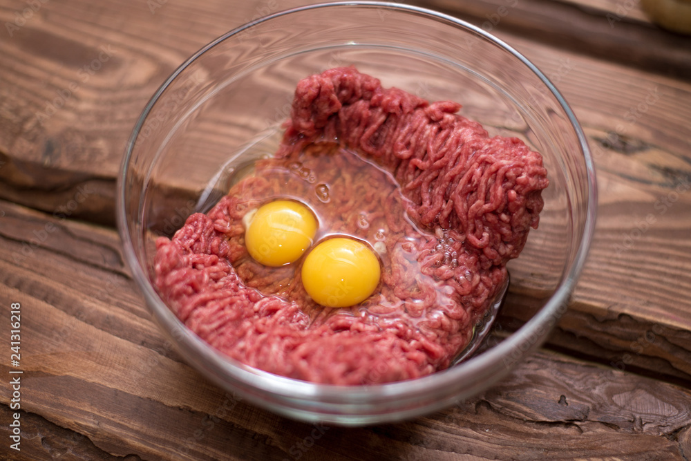 Fresh minced meat with chicken eggs on a plate on a wooden background for cooking. Fresh minced meat with chicken eggs on a plate on a wooden background for cooking.