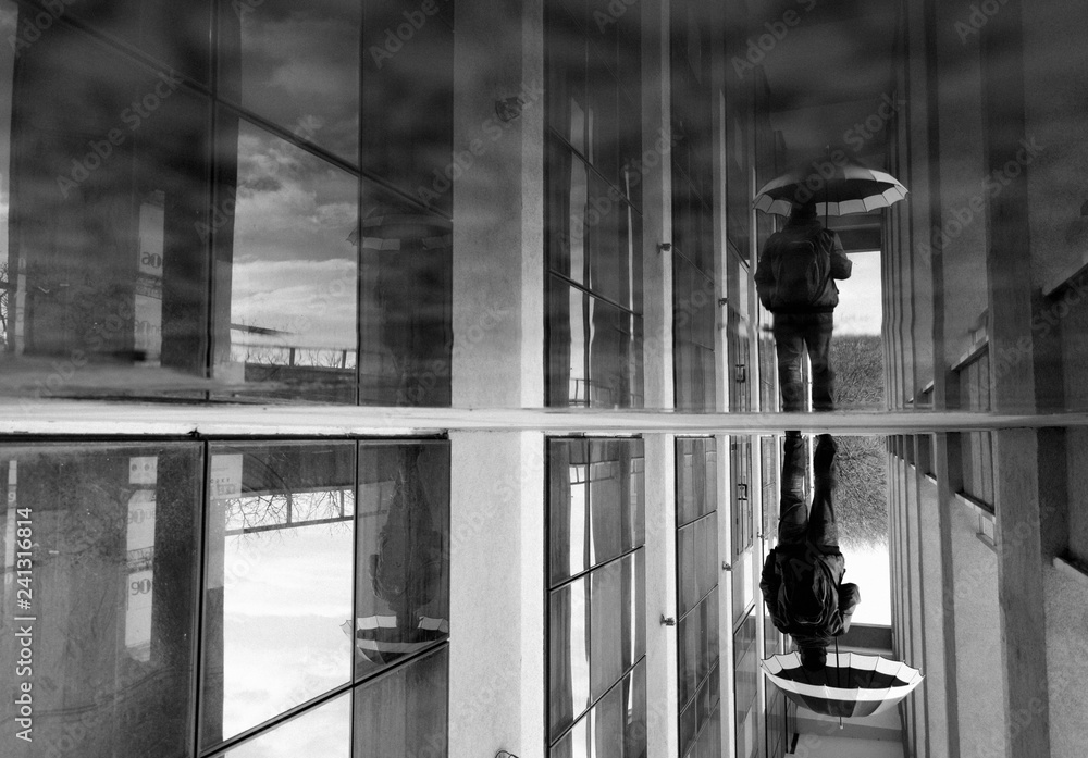 Obraz premium Street Photography - black and white reflection of a man with an umbrella.