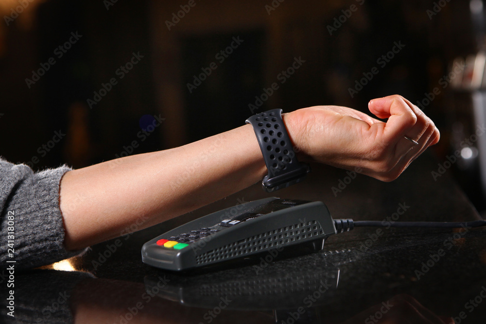 Payment for purchase hours through the terminal in the restaurant, shop. Women's hand close-up with a watch when paying for the purchase.