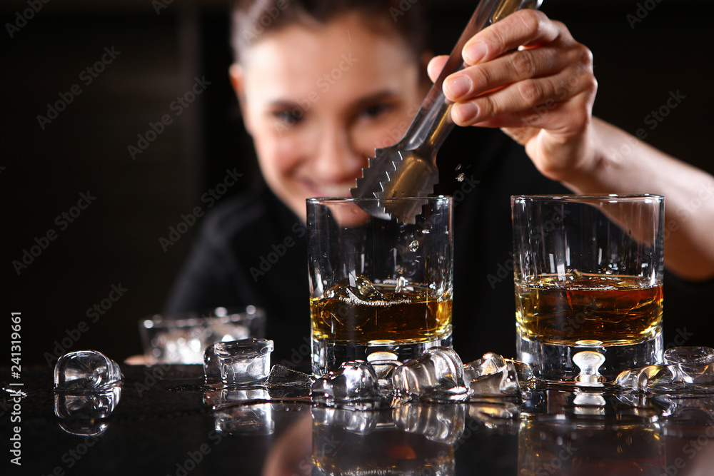 The bartender girl smiles and pours whiskey into glasses and adds ice. Photo on the bar in the restaurant. Girl out of focus.