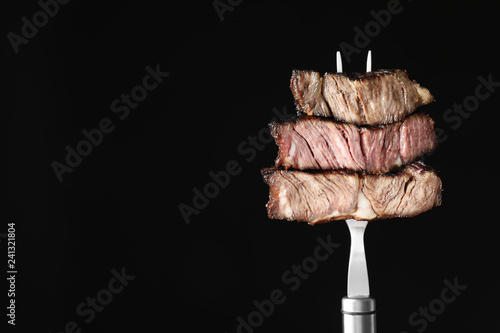 Fork with pieces of delicious barbecued meat on black background. Space for text