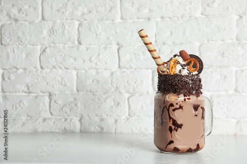 Mason jar of tasty milk shake with sweets on table near brick wall. Space for text photo