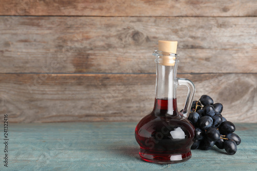 Glass jug with wine vinegar and fresh grapes on wooden table. Space for text