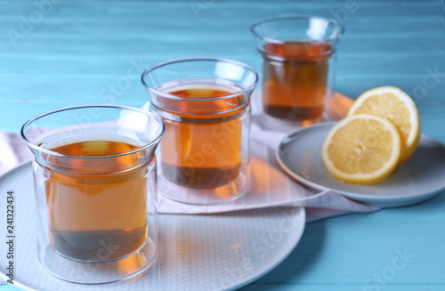 Plates with glasses of hot tea and lemon on blue wooden table