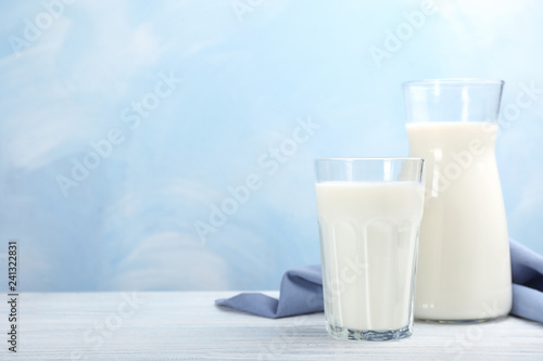 Glass and cruet with fresh milk on table against color background. Space for text