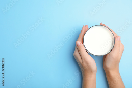 Woman holding glass of milk on color background, top view. Space for text