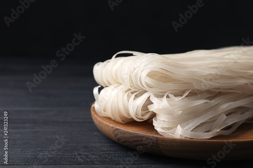 Plate with raw rice noodles on wooden table. Space for text