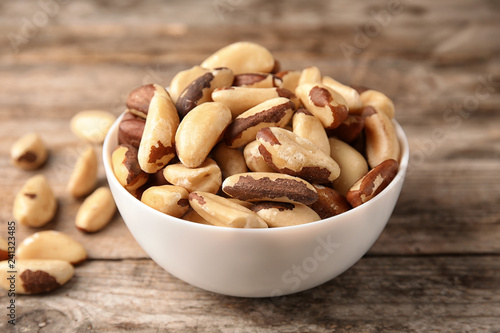 Bowl with tasty Brazil nuts on wooden background