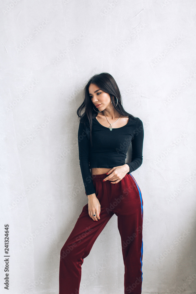 Portrait of a brunette girl in a cap and sportswear. Natural light. Red sweatpants, black top, black cap. Portrait of a brunette girl in a cap and sportswear. Natural light. Red sweatpants, black top, black cap.