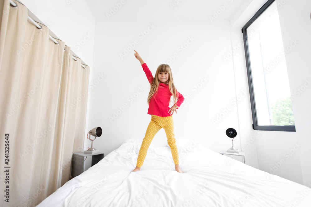 Little girl standing on bed with arm in the air Stock-Foto | Adobe Stock