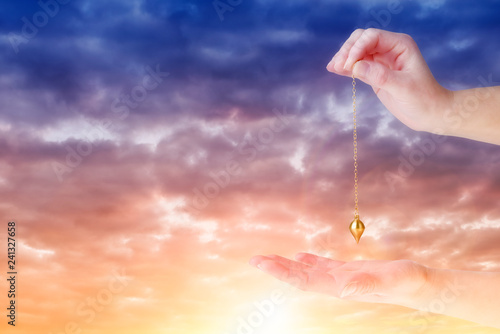 Close up of woman's hand holding a pendulum over her palm. Sunrise in background.