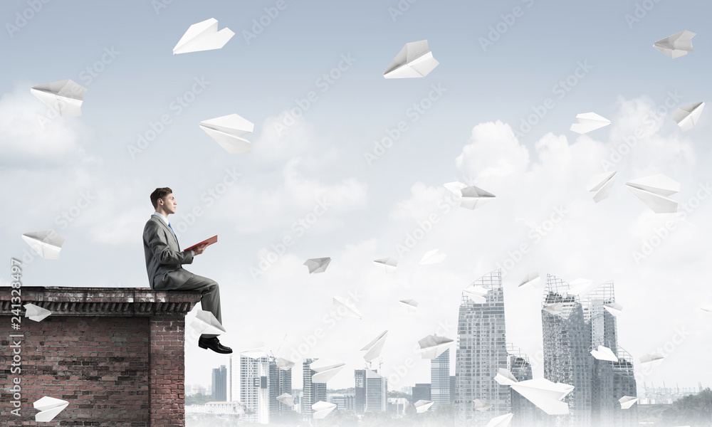 Man on roof edge reading book and cityscape at background Man on roof edge reading book and cityscape at background