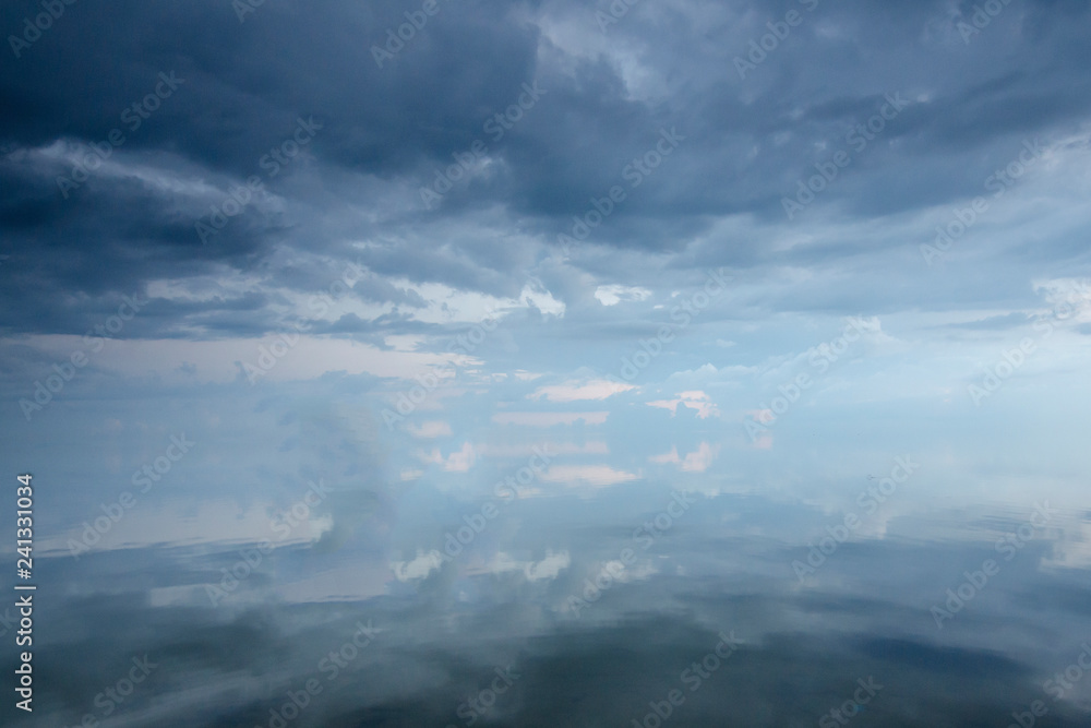 Obraz premium Textural clouds covered the sky over the ocean. The surface of the ocean is calm and reflects the clouds.