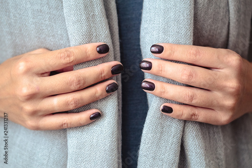 Gorgeous manicure, dark purple tender color nail polish, closeup photo. Female hands over simple background of casual clothes