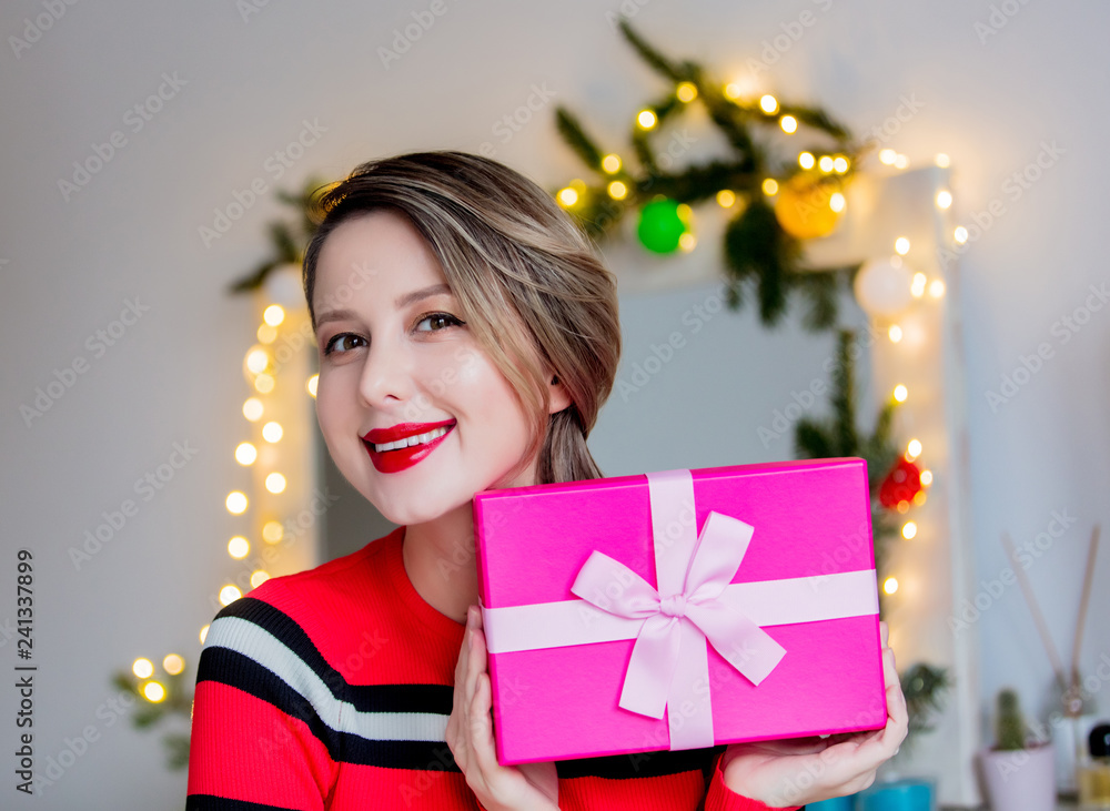 Beautiful woman in red sweater holding a gift box. Makeup mirror on background Beautiful woman in red sweater holding a gift box. Makeup mirror on background