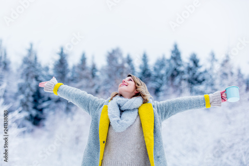 Beautiful girl in coat with cup of hot drink in a snow forest. Christmas of Valentine Day season time