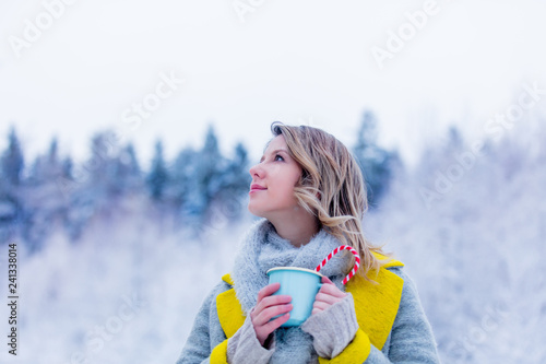 Beautiful girl in gray coat with cup of hot drink in a snow forest. Christmas of Valentine Day season time
