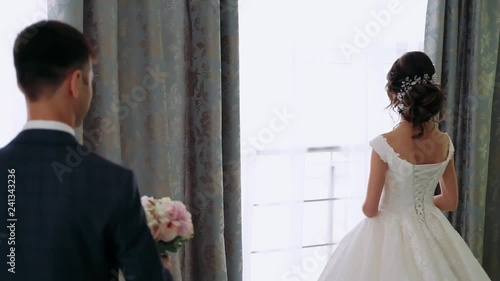 Groom meets happy bride first time seeing her in wedding dress silhouetted near window. Marrying couple embrace and kiss standing near huge window in room. close-up