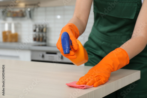 Female janitor cleaning table with rag in kitchen, closeup. Space for text