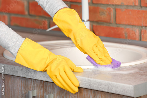 Woman cleaning kitchen sink with sponge, closeup