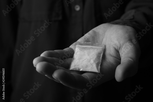 Drug dealer holding bag with cocaine, closeup. Black and white effect