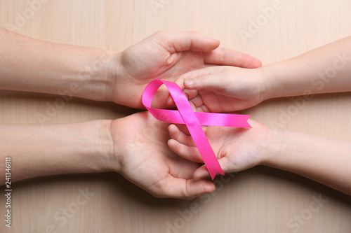 Woman and girl holding pink ribbon on wooden background  top view. Breast cancer awareness