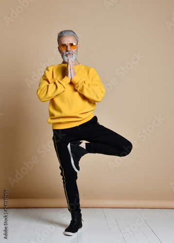 Fototapeta Naklejka Na Ścianę i Meble -  Portrait of happy senior millionaire man in yellow sunglasses stylish fashionable men practicing yoga asana stretching exercise 