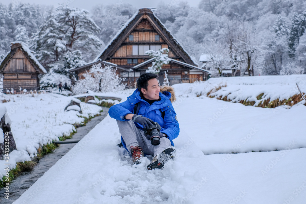 Asian man smiling face during snowing at Shirakawa-go village in winter including traditional House Gassho style and one of UNESCO world heritage sites, Gifu, Japan