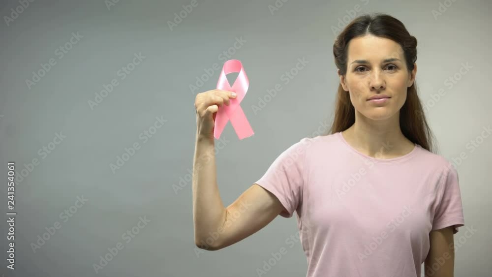 Woman showing pink ribbon into camera, international breast cancer awareness Woman showing pink ribbon into camera, international breast cancer awareness