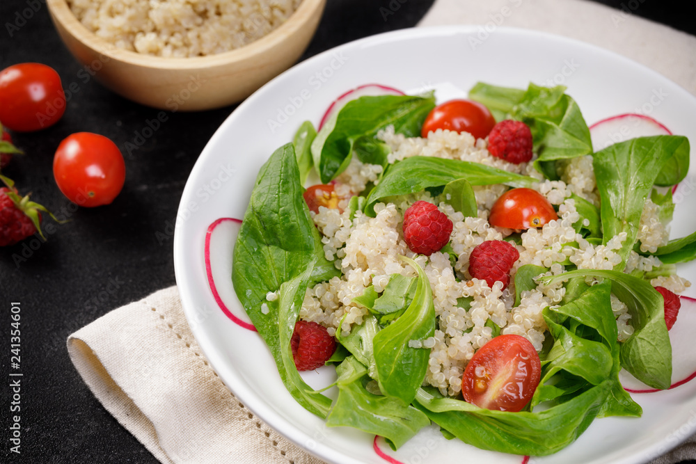 Quinoa salad with vegetables, raspberry and tomatoes on the black table. Super food for healthy and concept of balanced diet Quinoa salad with vegetables, raspberry and tomatoes on the black table. Super food for healthy and concept of balanced diet