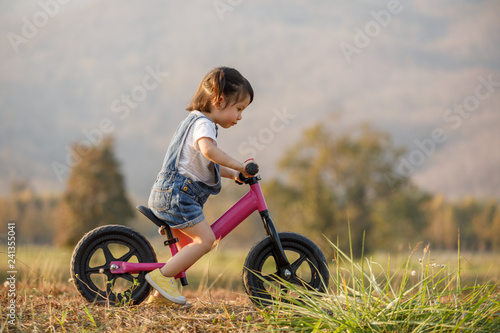 Happy child riding a bike. Little girl on a pink bicycle. Healthy preschool children summer activity. Kids playing outside. Little girl learns