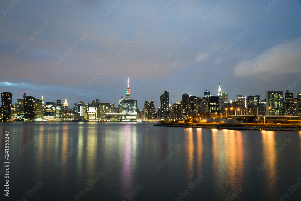 Skyline view of New York City near christmas time with the empire state building lit up in green and red to signify the festive time. sky is a light pale blue during golden hour time  