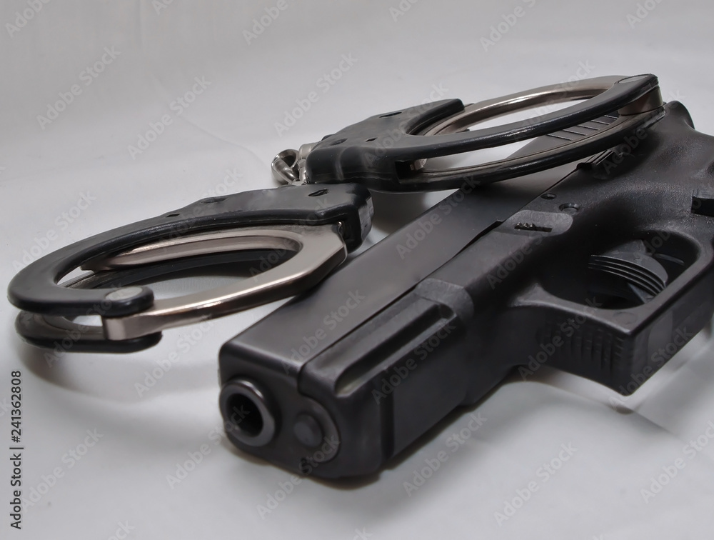 A pair of black and silver handcuffs laying on top of a black semi automatic pistol on a white background