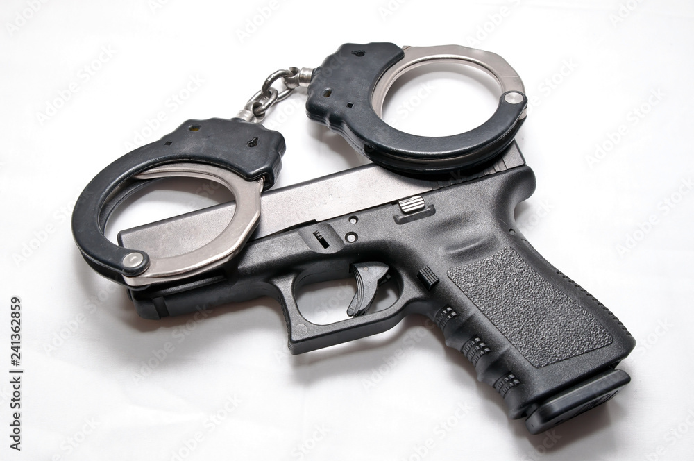 A pair of black and silver handcuffs laying on top of a black semi automatic pistol on a white background A pair of black and silver handcuffs laying on top of a black semi automatic pistol on a white background