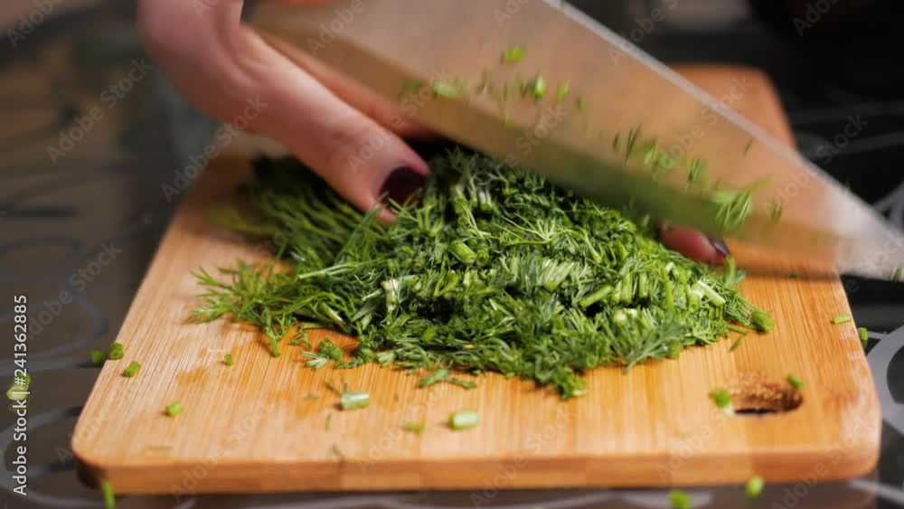 Cutting dill. Female hands cut dill with a large knife on a wooden cutting board. Close-up Cutting dill. Female hands cut dill with a large knife on a wooden cutting board. Close-up
