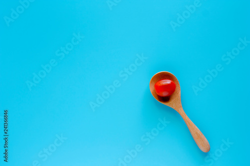 Fresh red tomato in wooden spoon on blue background for diet and heathy eating concept