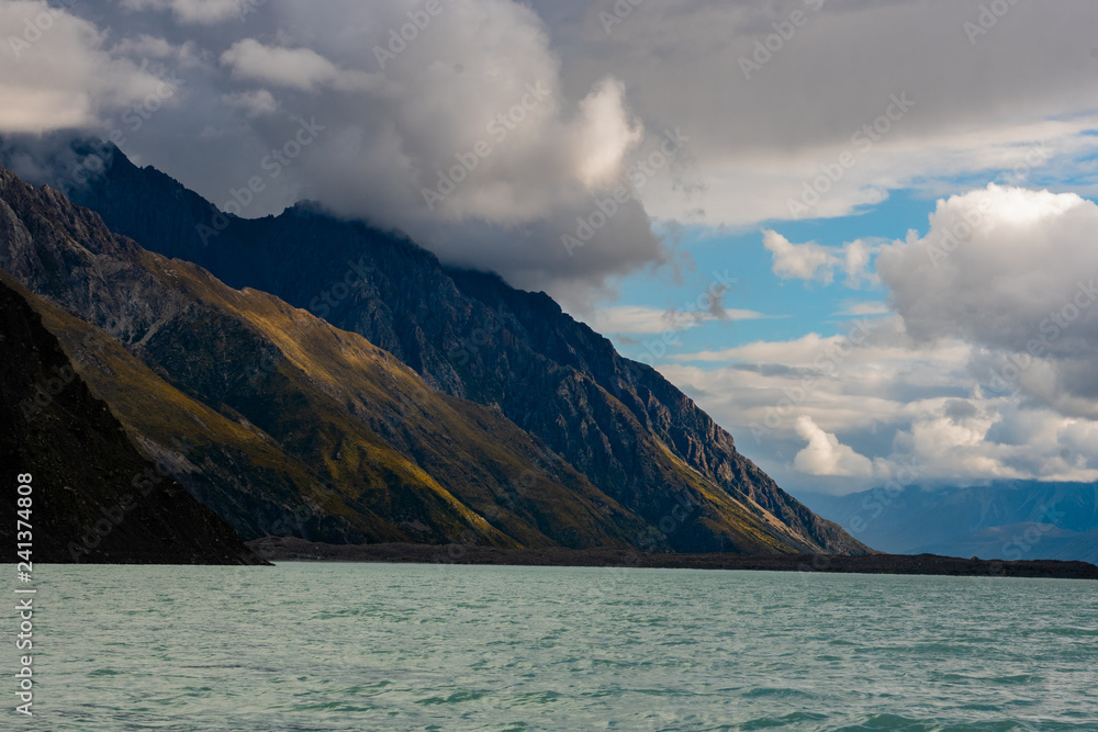 The Sun Peaks Through Clouds and Beautifully Lights up the Mountain Side - Tasman Lake New Zealand