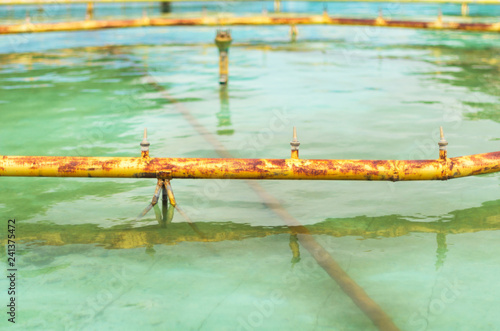 Rusted yellow pipes and water jets of a fountain drained for maintenance or servicing on a summer day.