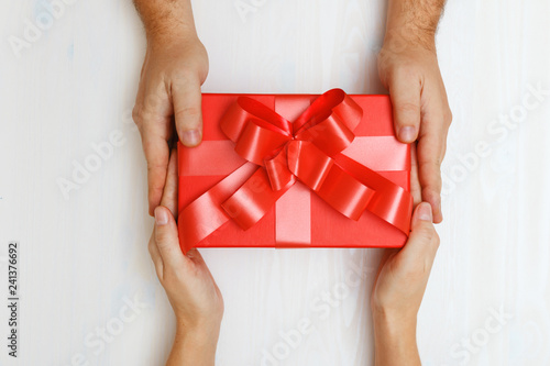 Closeup of a man's hand giving a red box with a gift to a woman. Top view. Concept of Valentine's Day and Christmas celebration