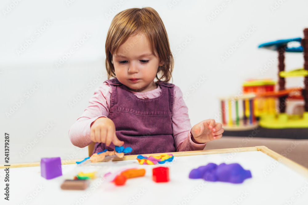 Kid girl is playing with plasticine while sitting at table in nursery room. Kid girl is playing with plasticine while sitting at table in nursery room.