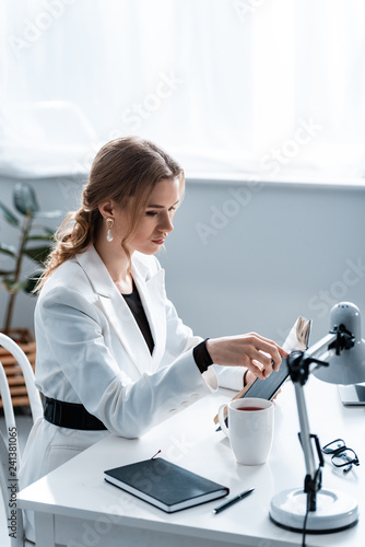 focused businesswoman in formal wear sitting at desk and reading notebook at workplace