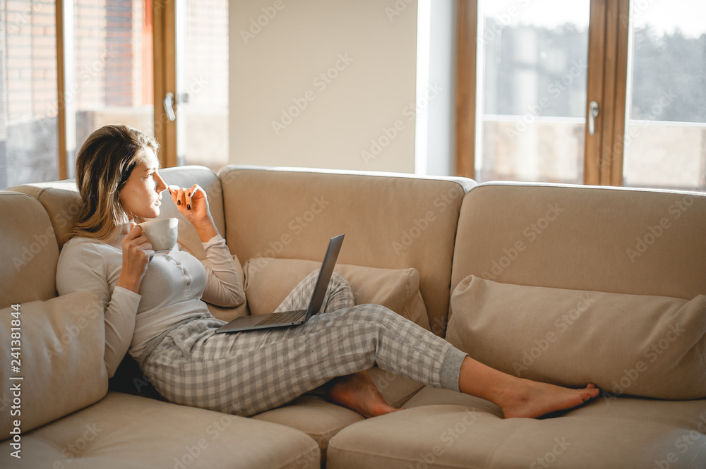 Beautiful girl writes an article or a book while sitting on the couch with a laptop. Cozy home atmosphere and warm morning light Beautiful girl writes an article or a book while sitting on the couch with a laptop. Cozy home atmosphere and warm morning light