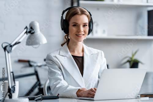 smiling businesswoman in headphones sitting at computer desk at workplace