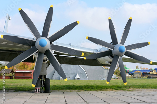 Retro plane with propellers on blue sky background. Airplane details with clouds. Aviation transport on airfield. Black propeller blade with yellow on the top. Jet engine of an vintage airliner.