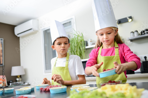 beautiful young happy kids boy and girl cooking and baking a cake in kitchen at home
