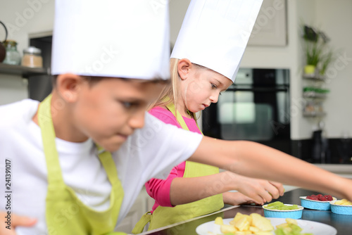beautiful young happy kids boy and girl cooking and baking a cake in kitchen at home