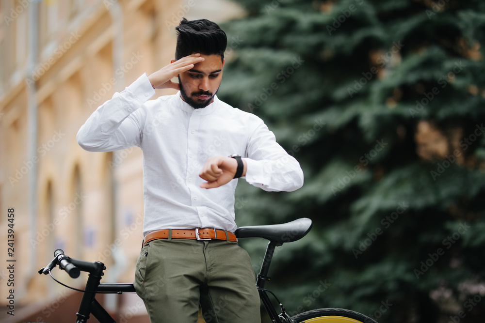 Smart and confident indian businessman looking at his watch while late to meet by bicycle, copy space